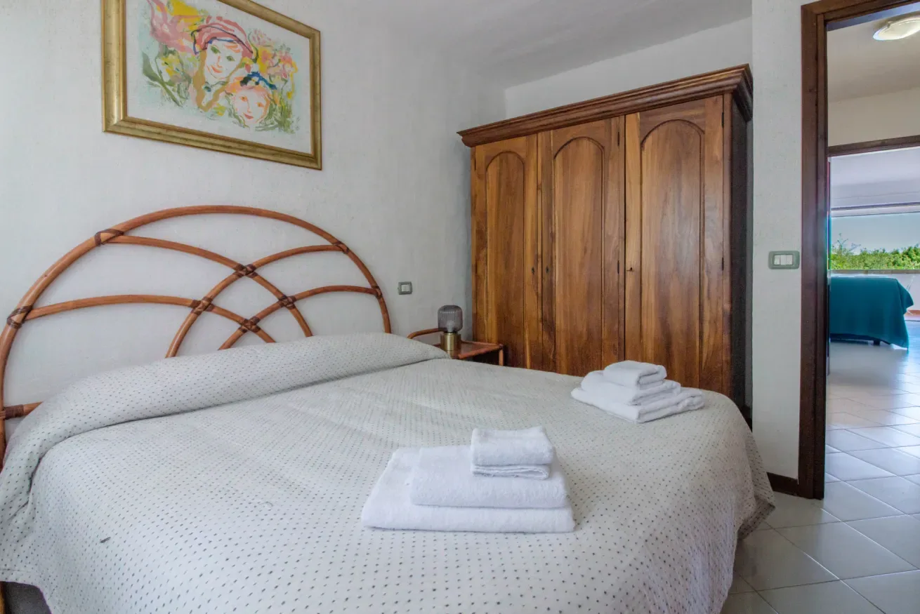 A bedroom with a bed, folded towels, and a wooden wardrobe.