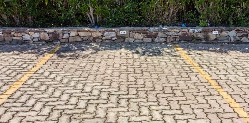 A paved outdoor parking area with yellow lines in front of a low stone wall.