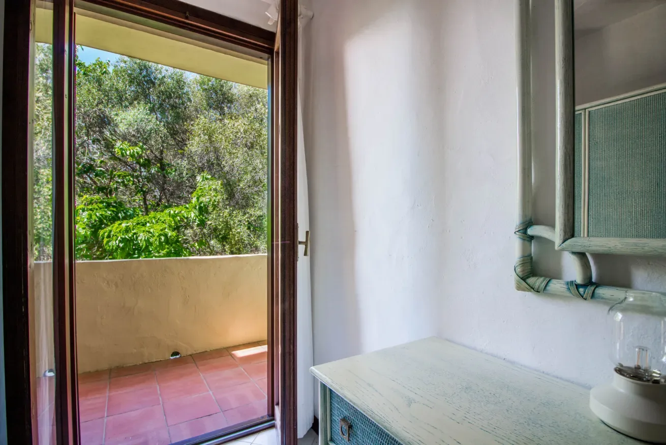 A bathroom vanity sits beside an open doorway leading to a leafy balcony.