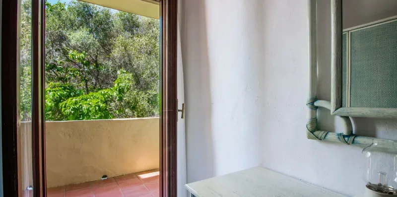A room opens onto a small balcony overlooking leafy trees.