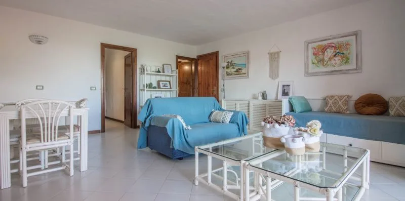 A bright living room with blue seating, a glass coffee table, and a dining table.