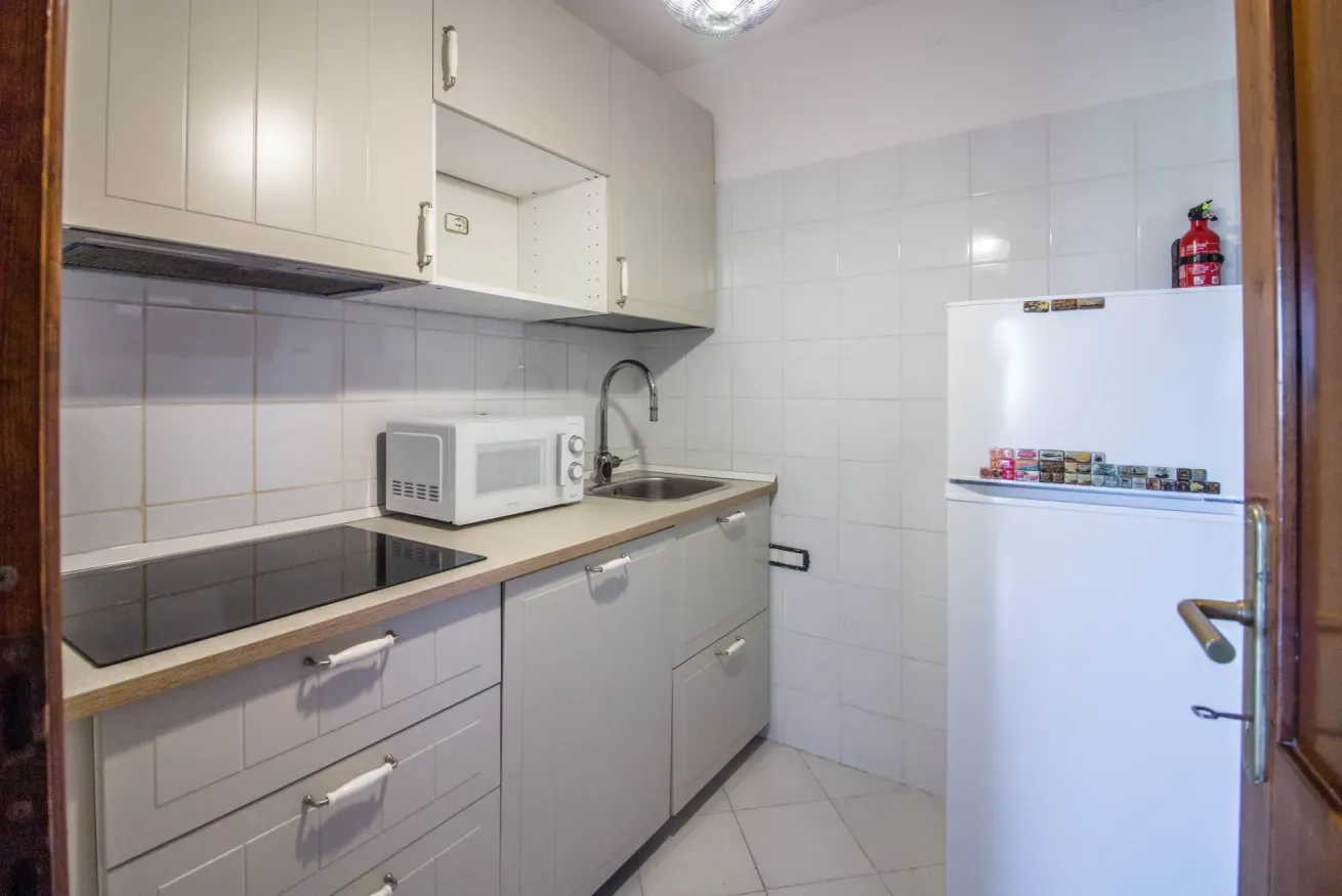 A compact kitchen with white cabinets, a countertop, and a refrigerator.