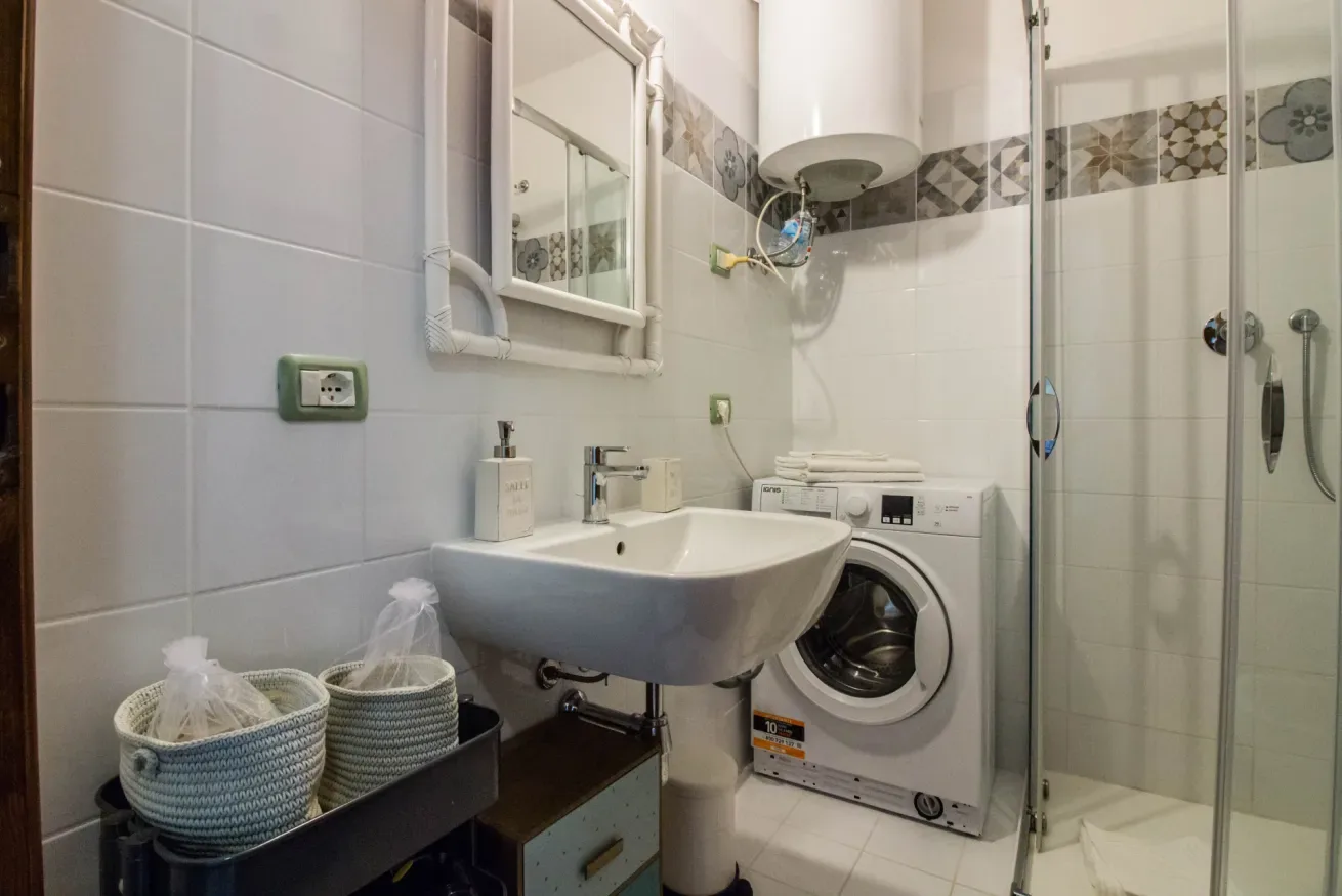 A tiled bathroom with a sink, washing machine, and glass shower.