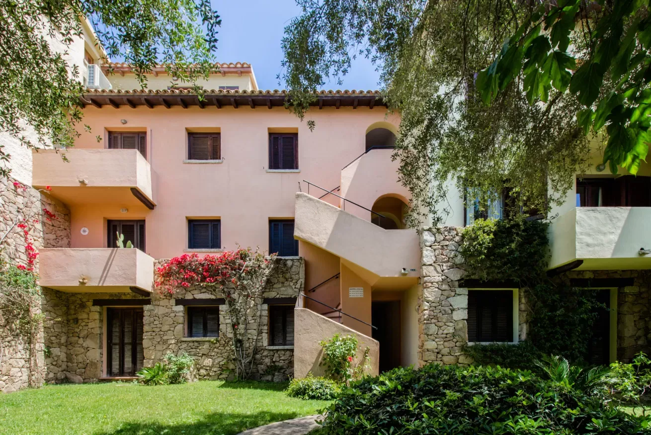 A pink multi-story building with exterior staircases stands behind a green lawn.