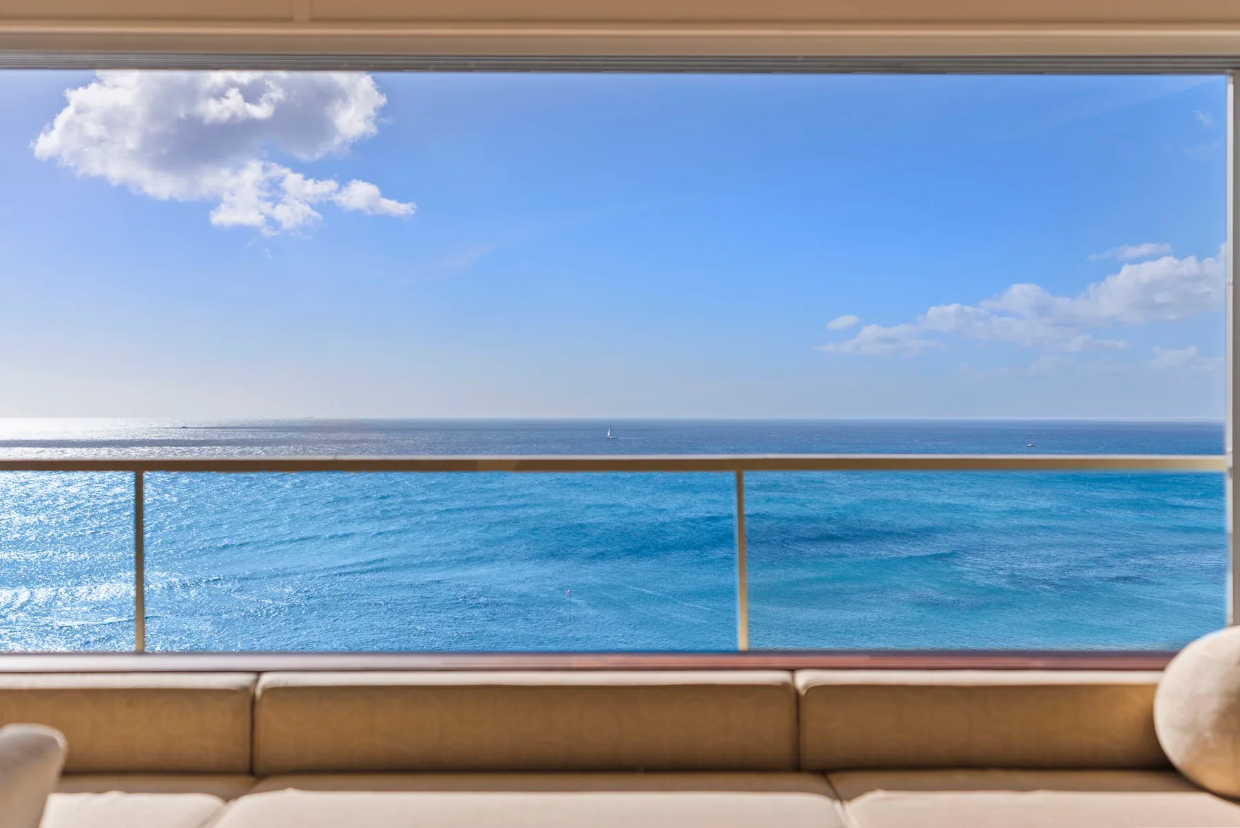 Una zona de estar en un balcón ofrece vistas al mar azul bajo un cielo parcialmente nublado.