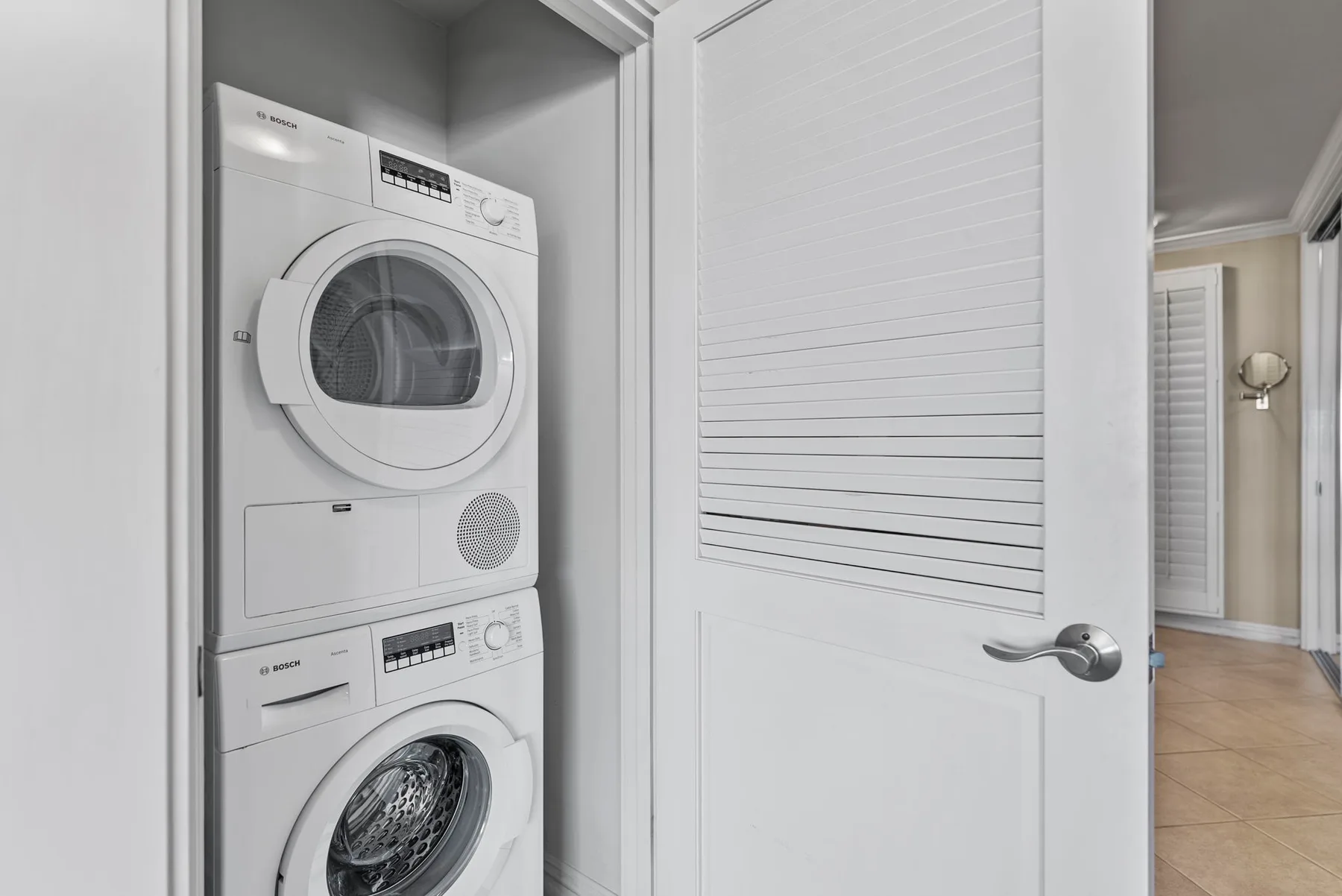 Zona de lavandería con lavadora y secadora apiladas detrás de una puerta abierta.
