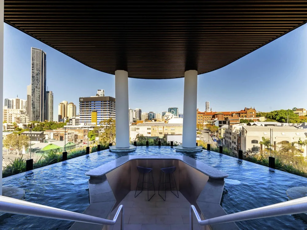 Una terraza en la azotea con una piscina poco profunda y edificios de la ciudad al fondo.