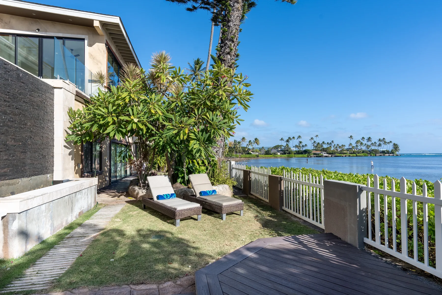 Outdoor patio with lounge seating beside a white fence overlooking the water.