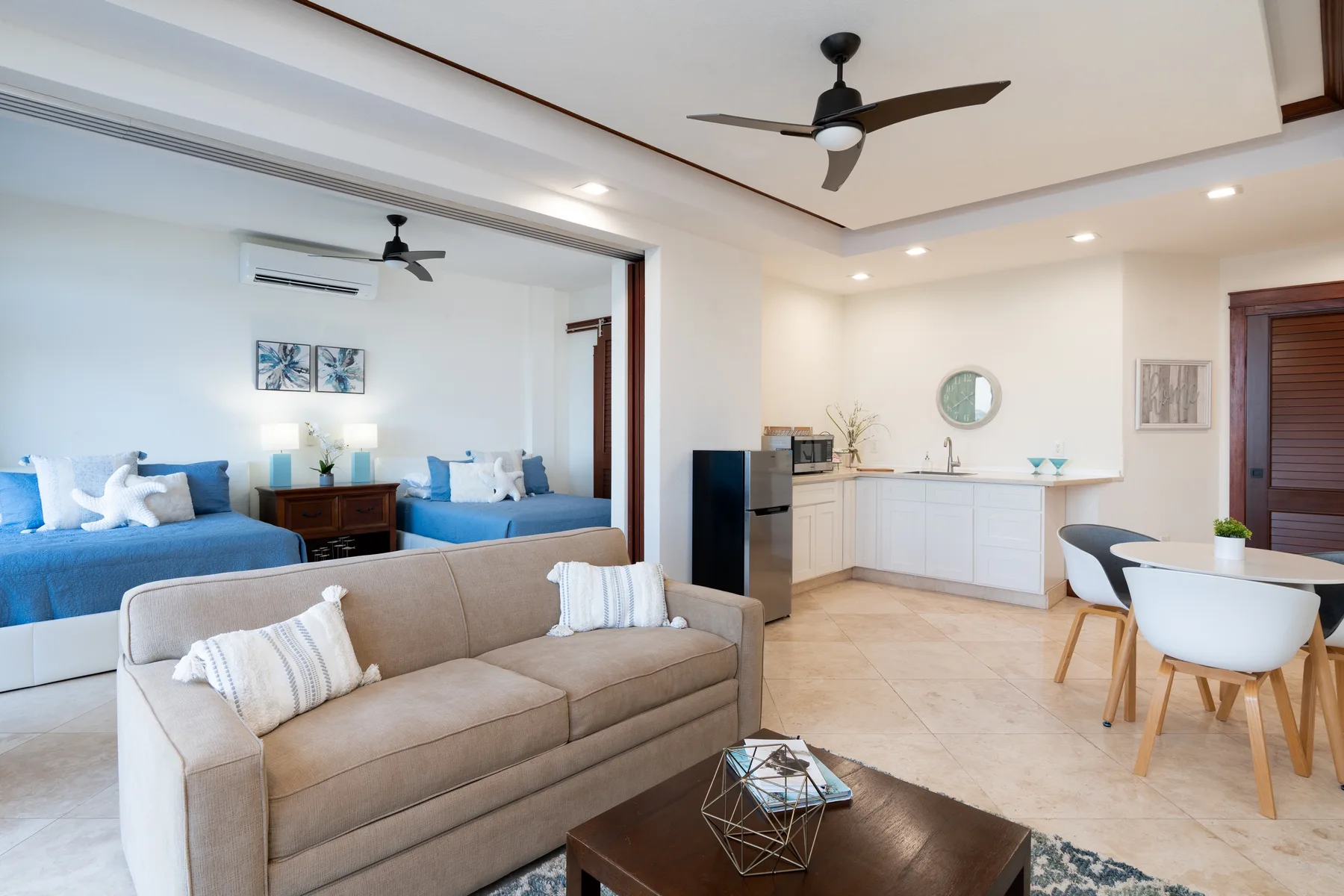 A bright living area with a sofa, blue seating, and a compact kitchen.
