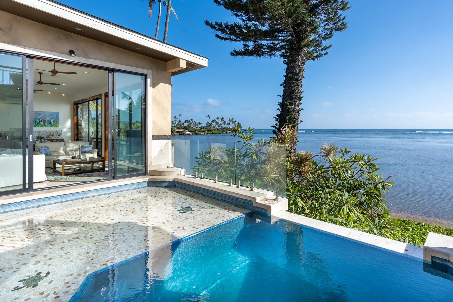 A swimming pool beside a glass-fronted living area overlooks the ocean.