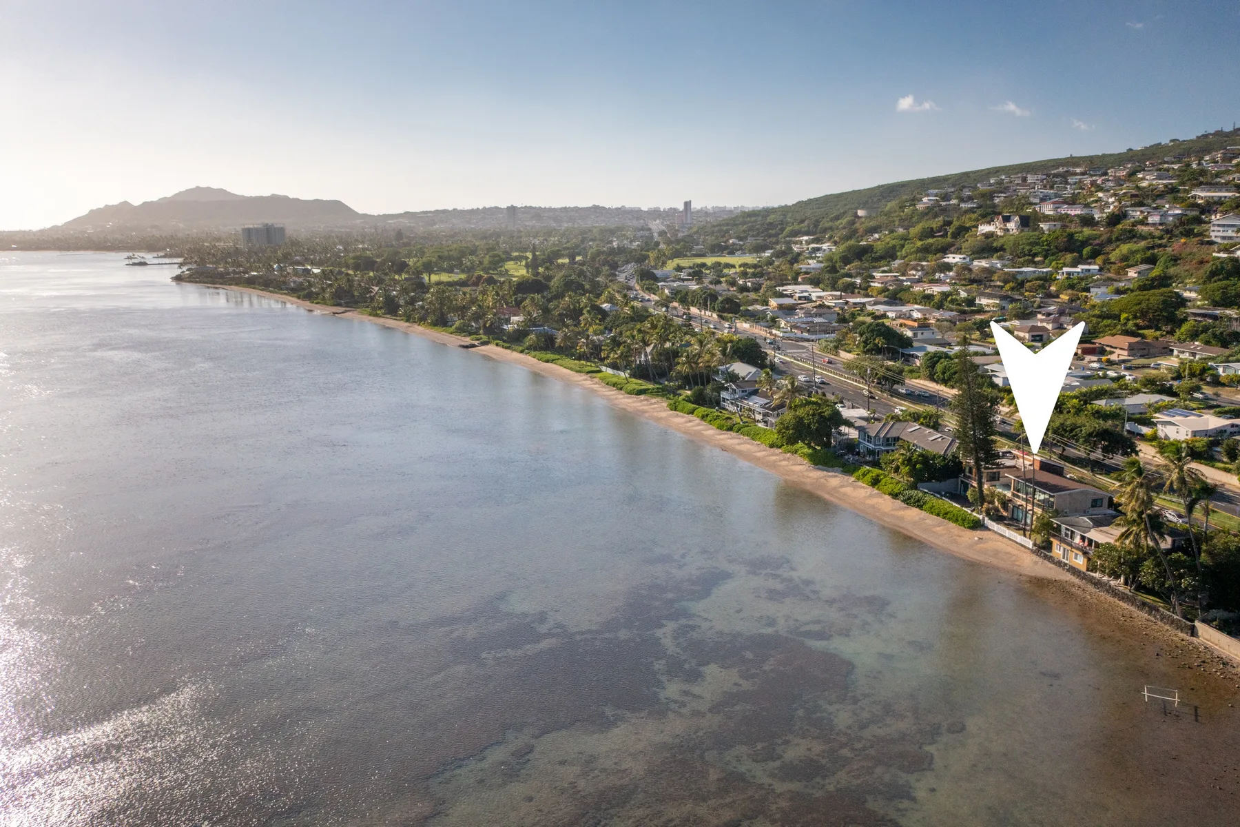 Coastal shoreline with calm water and homes along a green hillside.