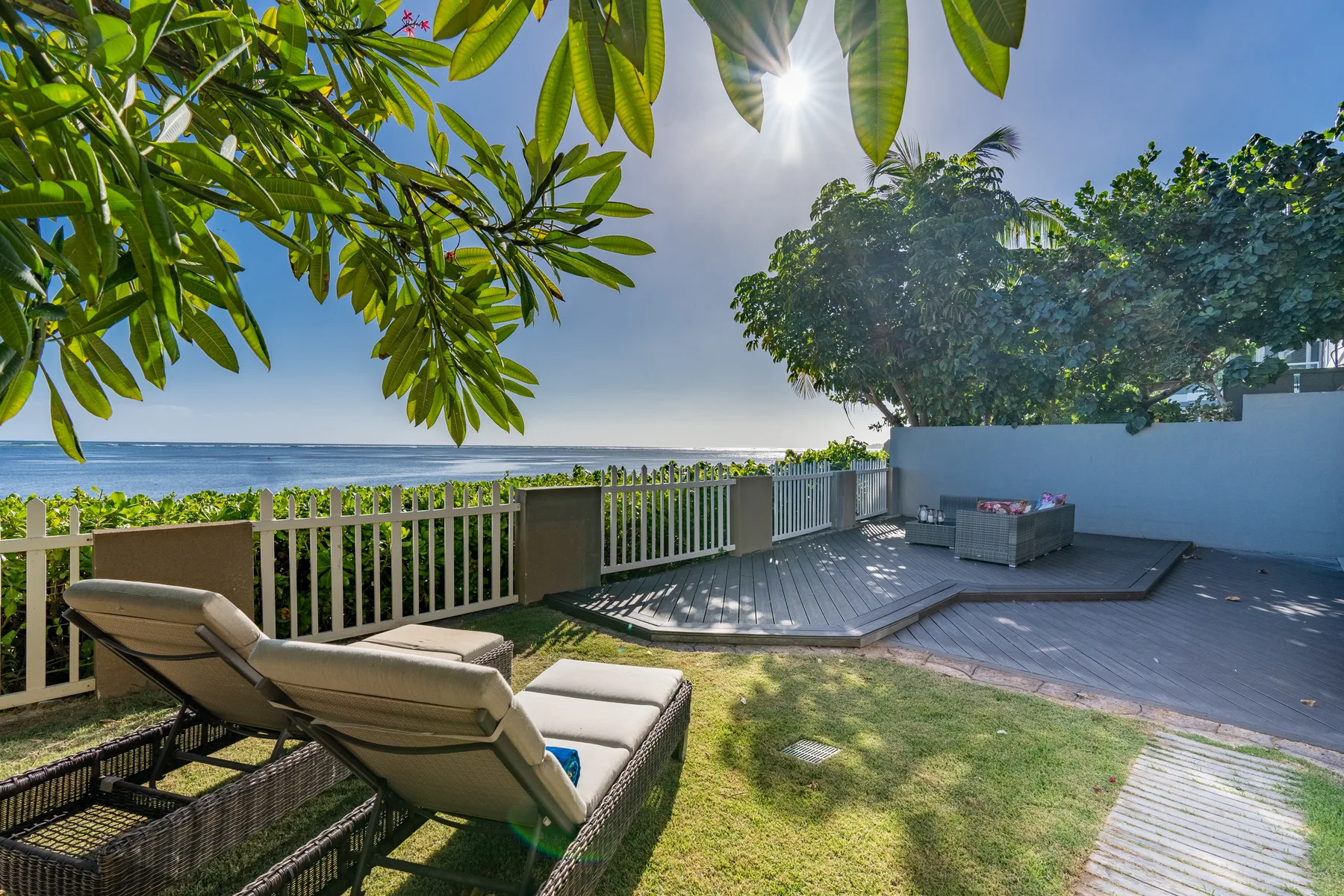 A sunny outdoor patio overlooks the water, with lounge seating beside a raised deck.