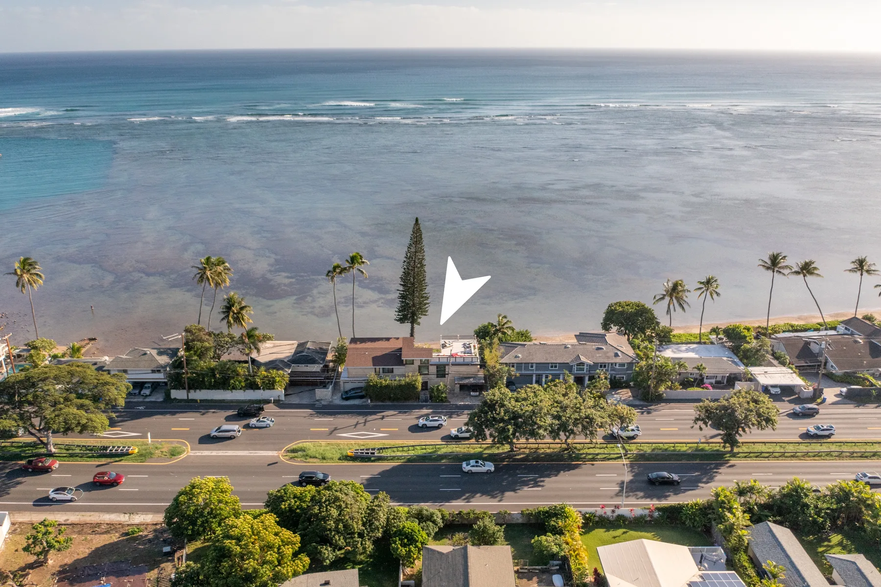 An aerial view shows a coastal road, buildings, and the ocean beyond.