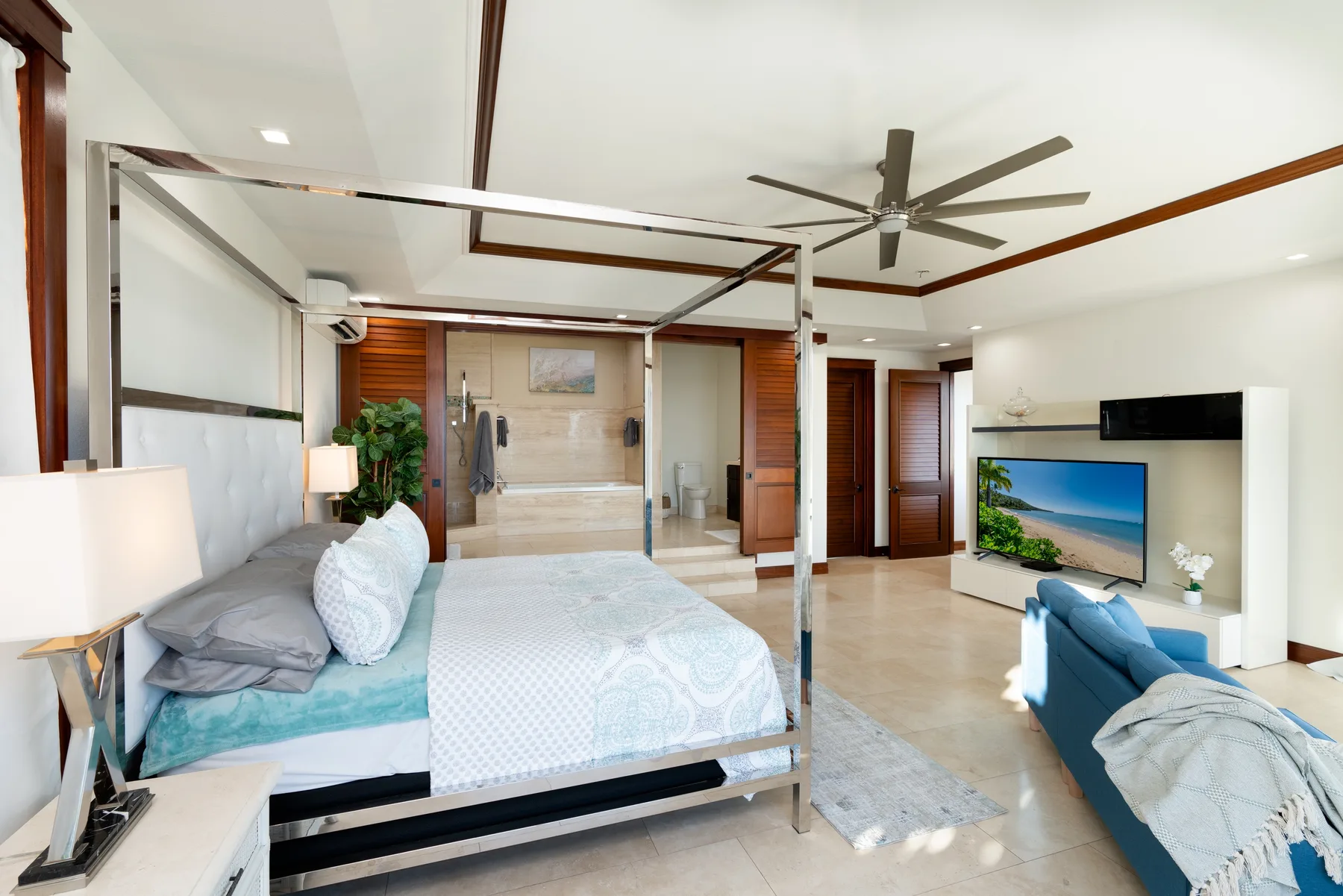 A bedroom with a large bed, a ceiling fan, and a television area.
