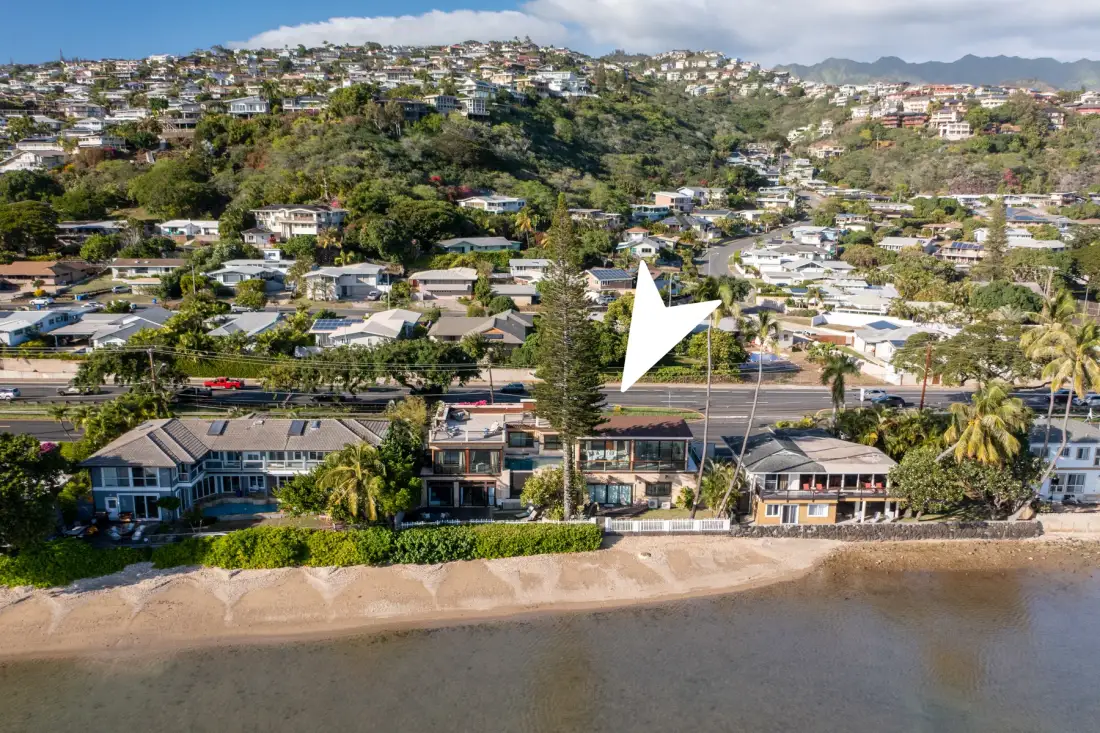 Aerial view of homes along a sandy shoreline with hills in the background.