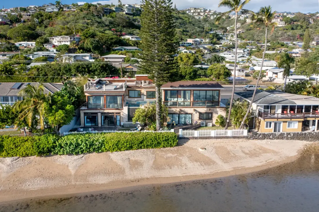 Houses line a sandy beach, with a green hillside rising behind them.