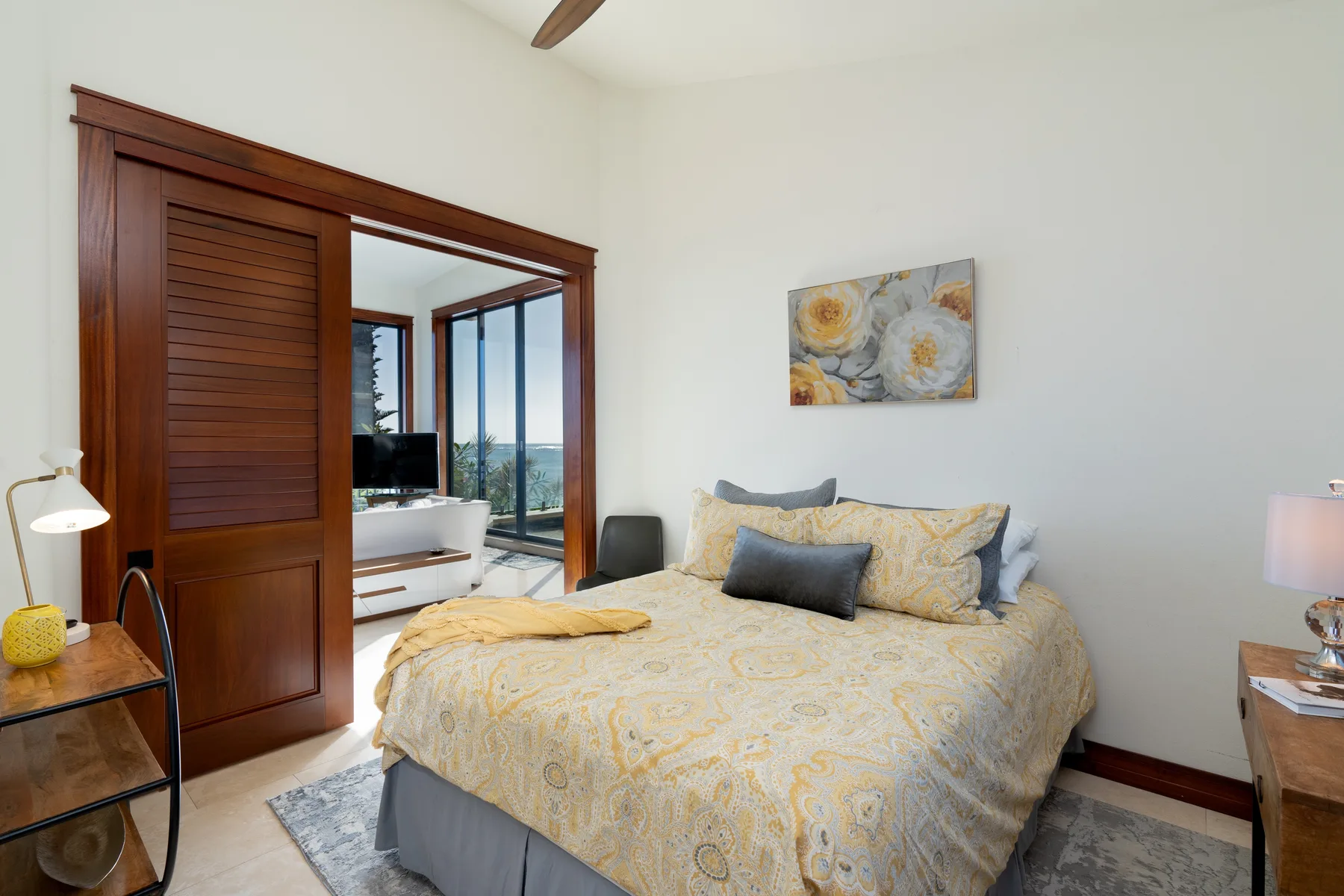 A bedroom with a bed dressed in pale patterned bedding and wall art.
