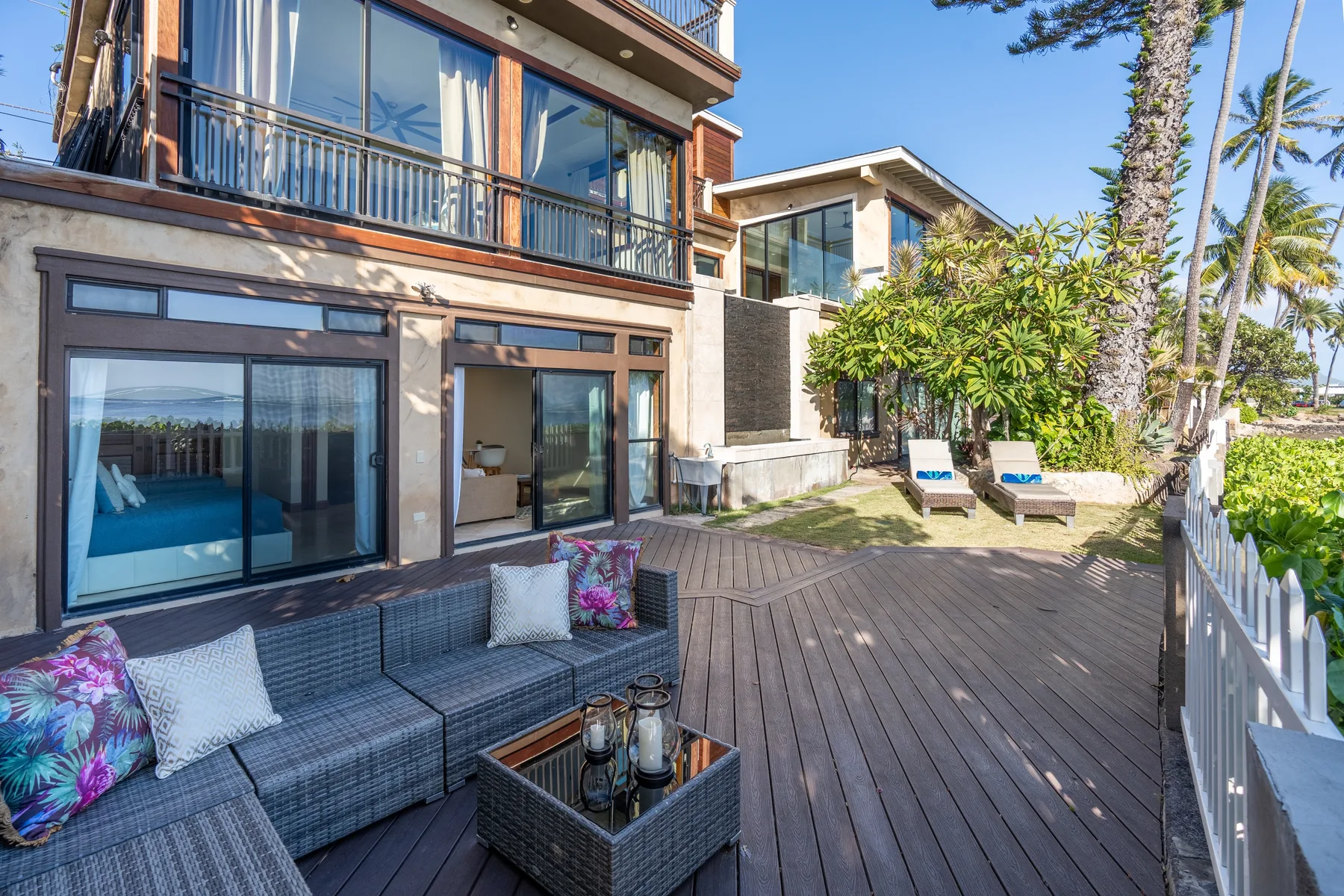A modern house opens onto a wooden deck with outdoor seating and greenery.