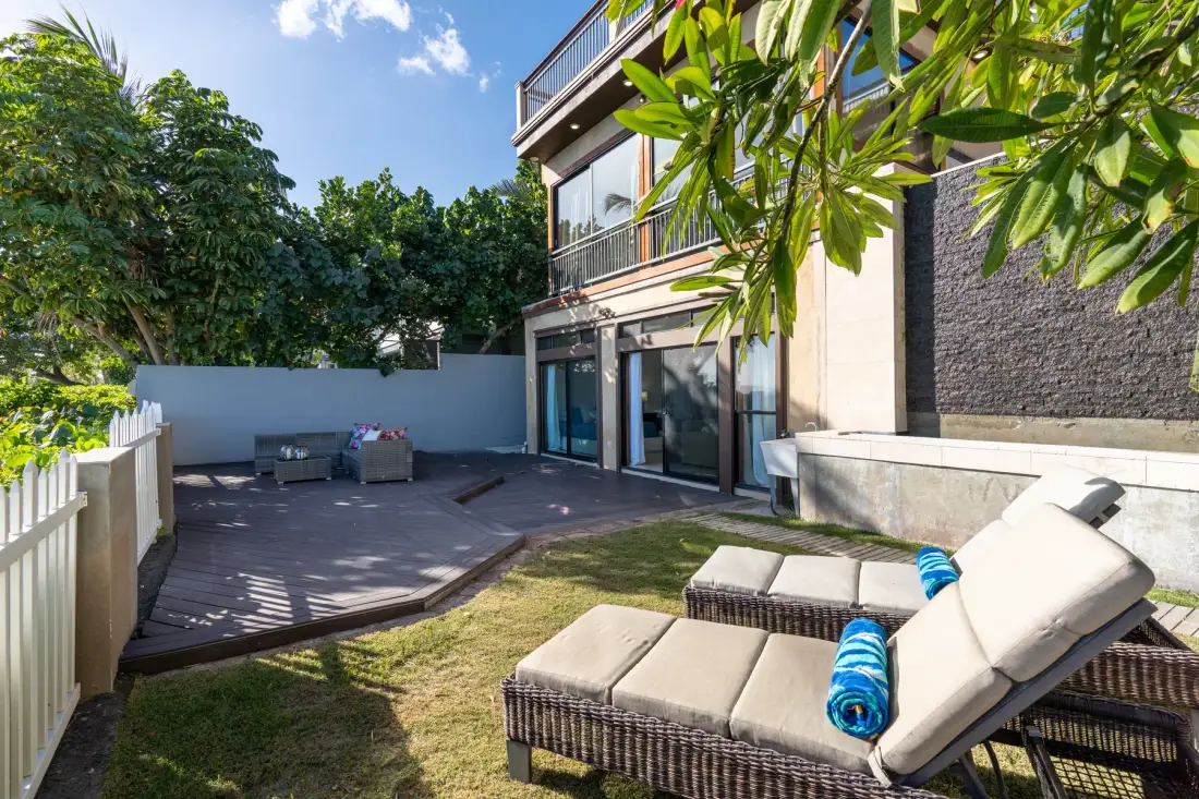 An outdoor patio beside a modern house, with cushioned lounge seating and a small lawn.