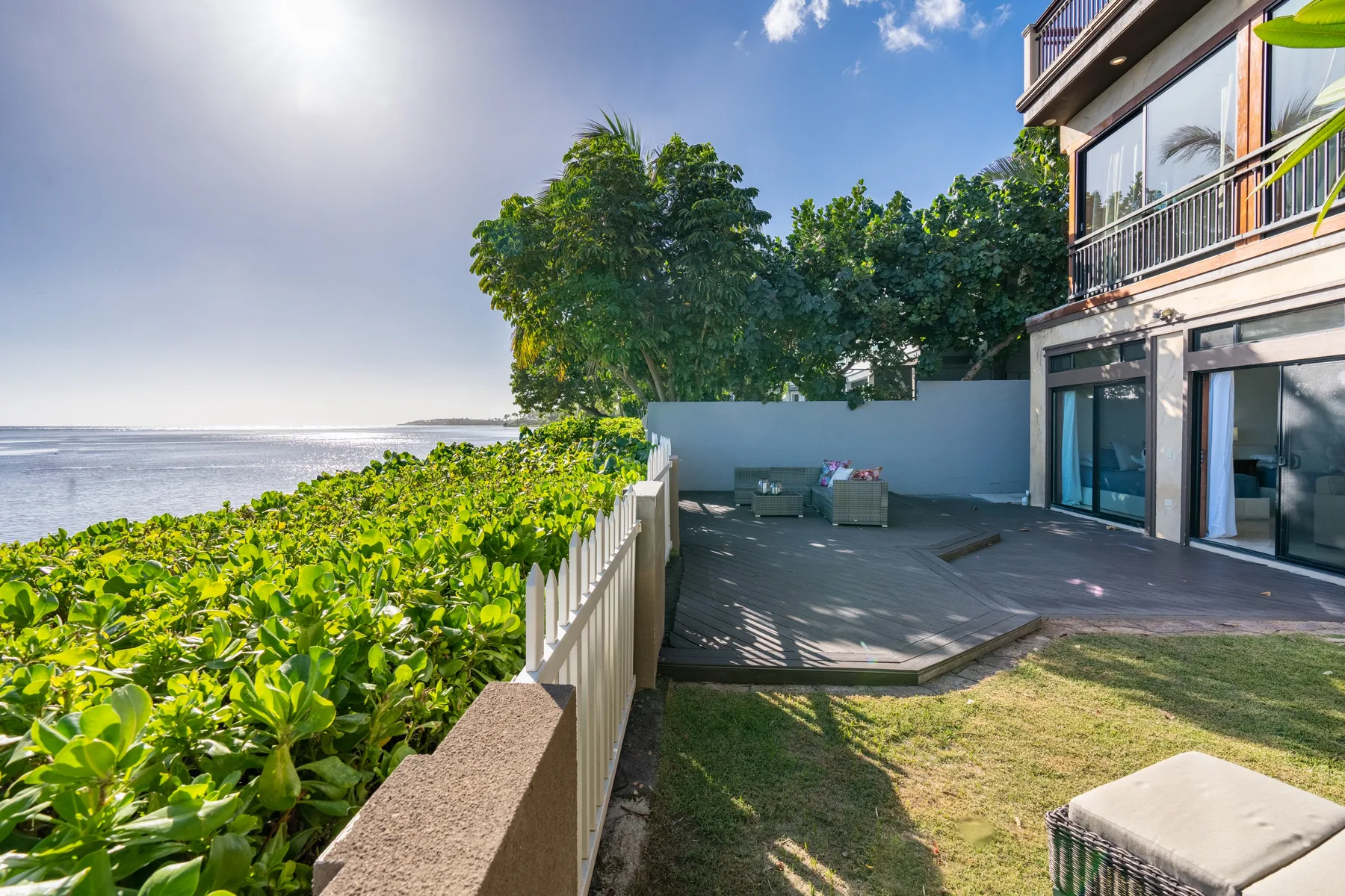 A seaside patio beside a modern building, with greenery along the edge.