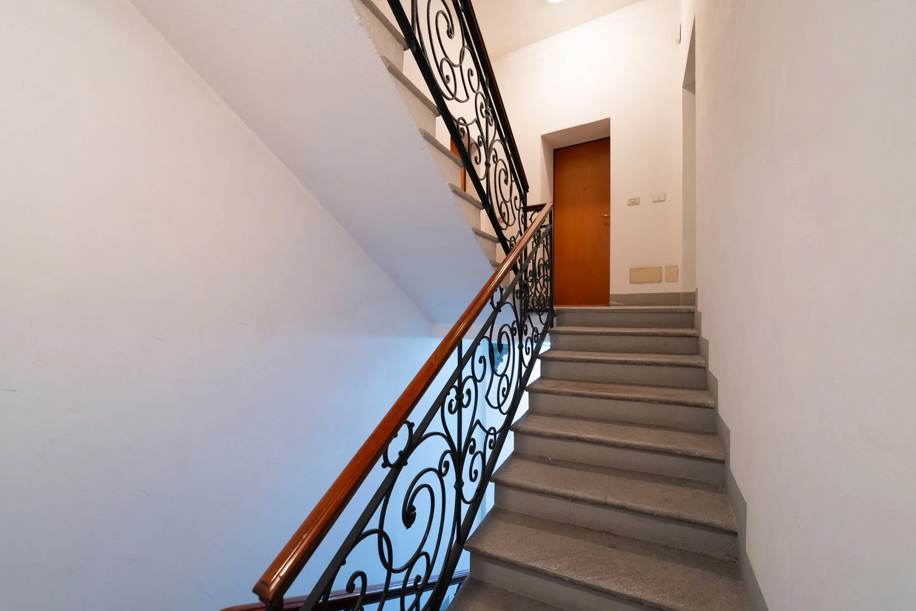 Una escalera interior con barandillas metálicas decorativas conduce a una puerta de madera.