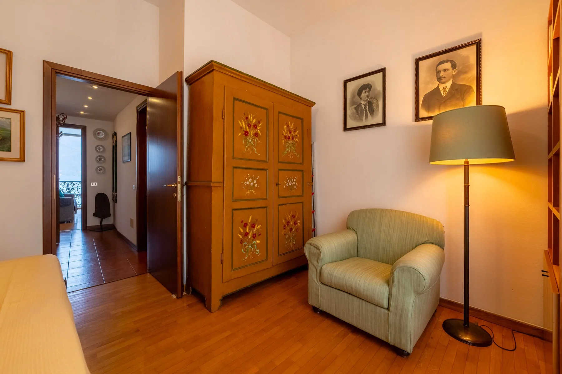 Un dormitorio cálidamente iluminado con un armario de madera, un sillón y una lámpara de pie.