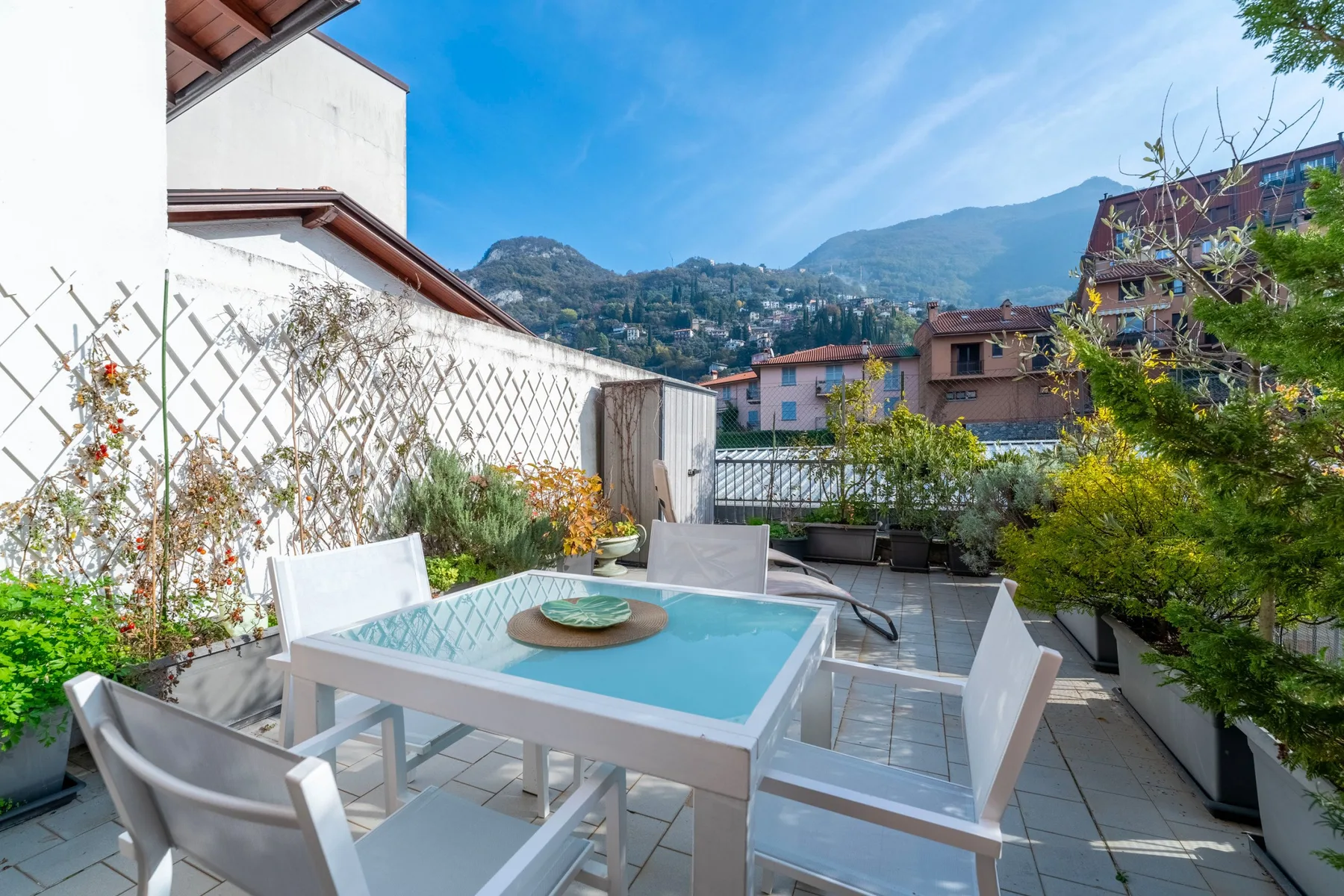 Una terraza exterior embaldosada tiene una mesa y asientos con vistas a casas en la ladera.