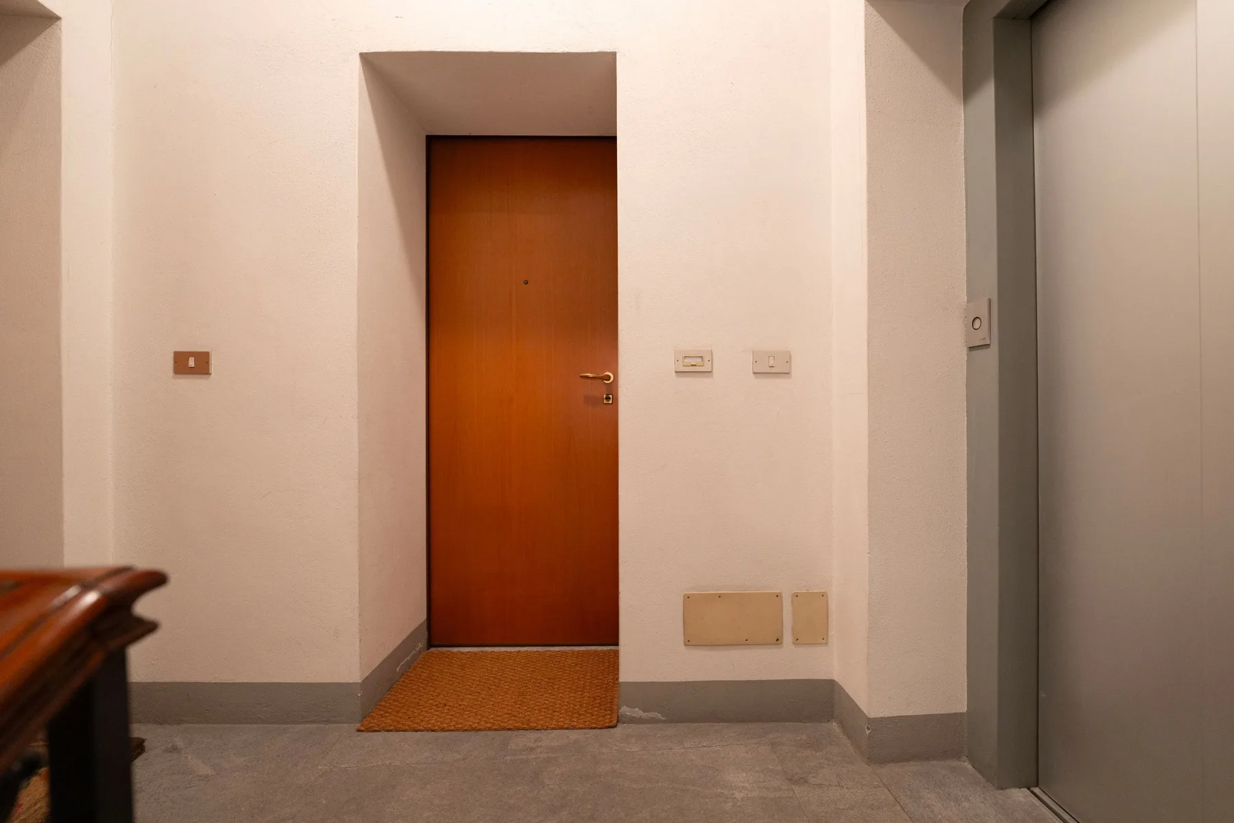 Un pasillo interior con una puerta de madera cerrada y una puerta gris de ascensor.