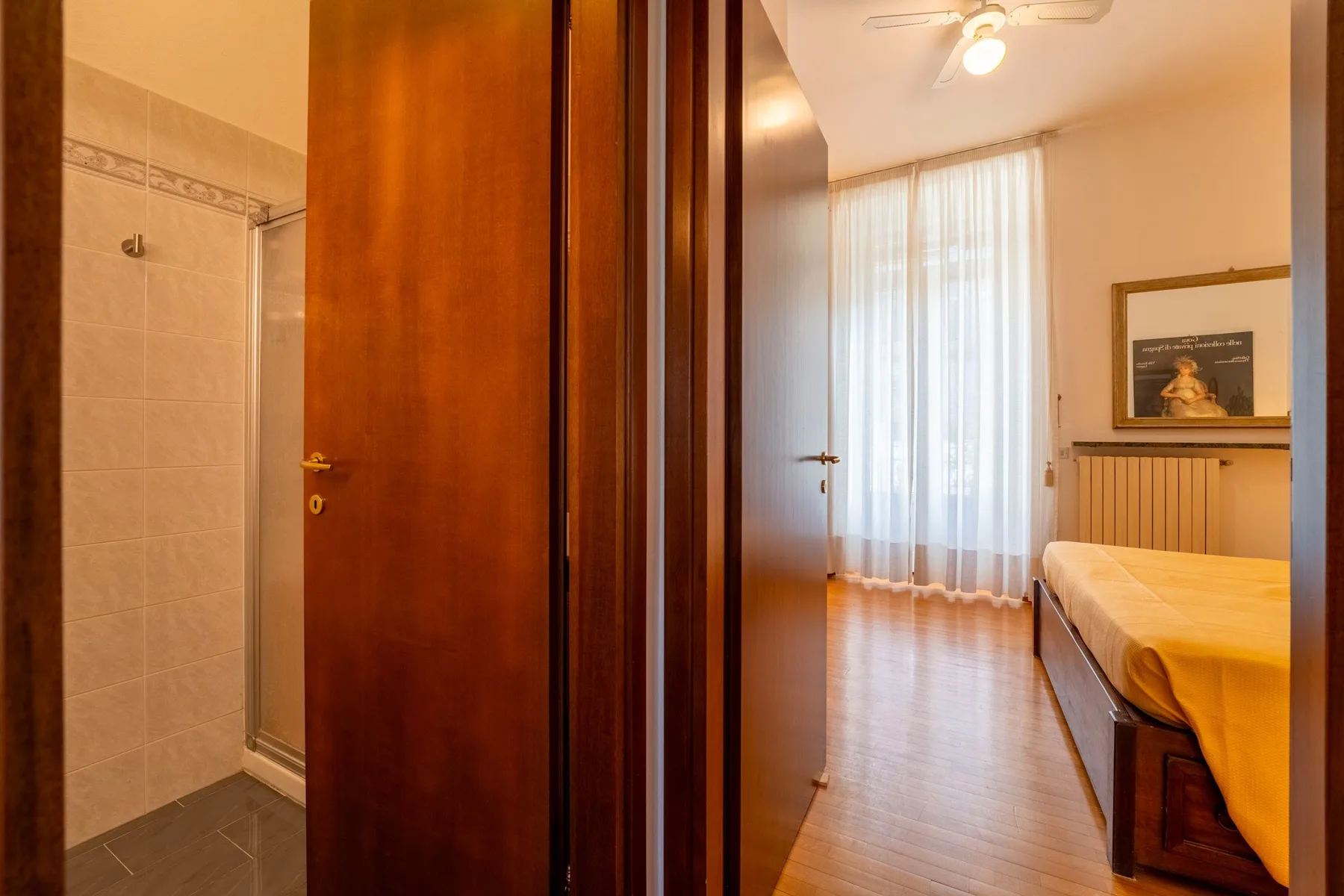 Dormitorio con una cama junto a una ventana amplia con cortinas, visto desde una puerta abierta.