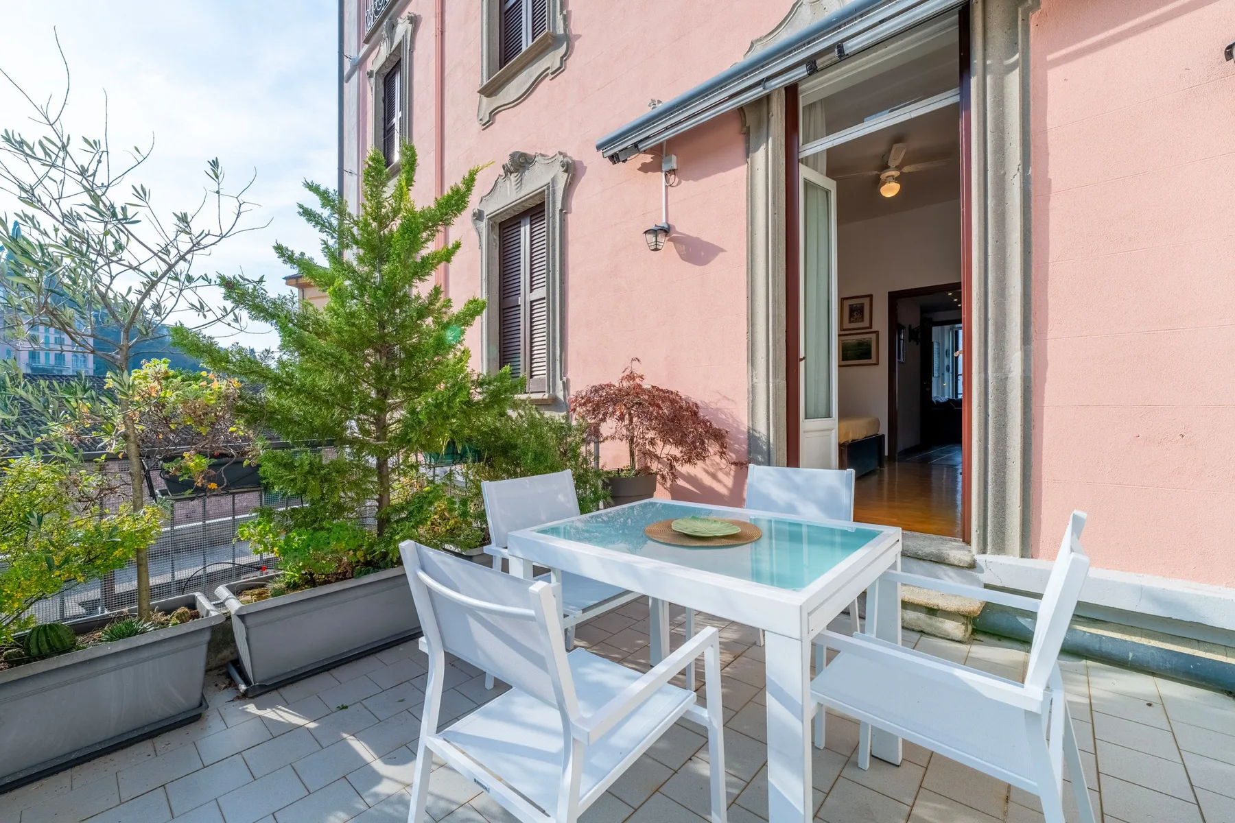 Un patio exterior con una mesa de comedor y asientos junto a un edificio rosa.