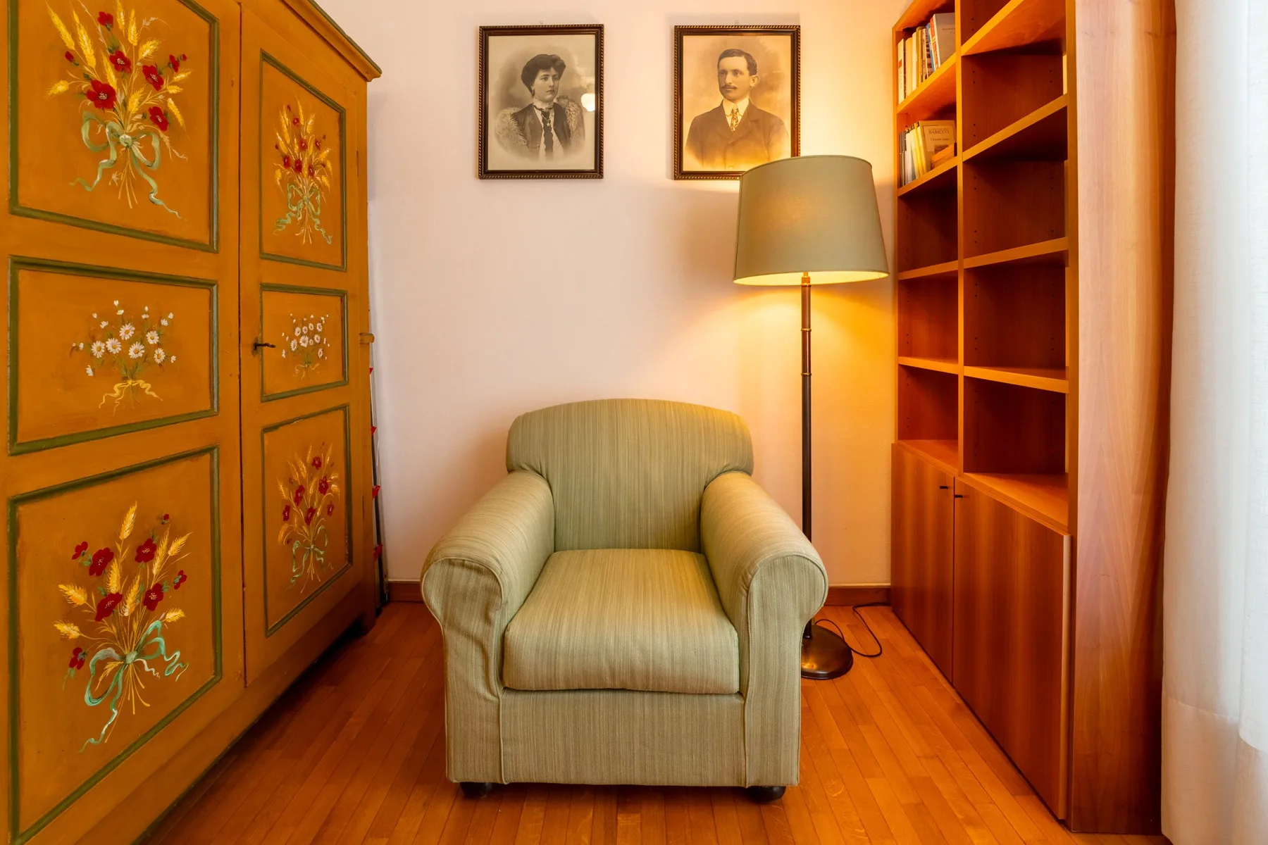 Una habitación amueblada con un sillón tapizado entre un armario pintado y estanterías de madera.