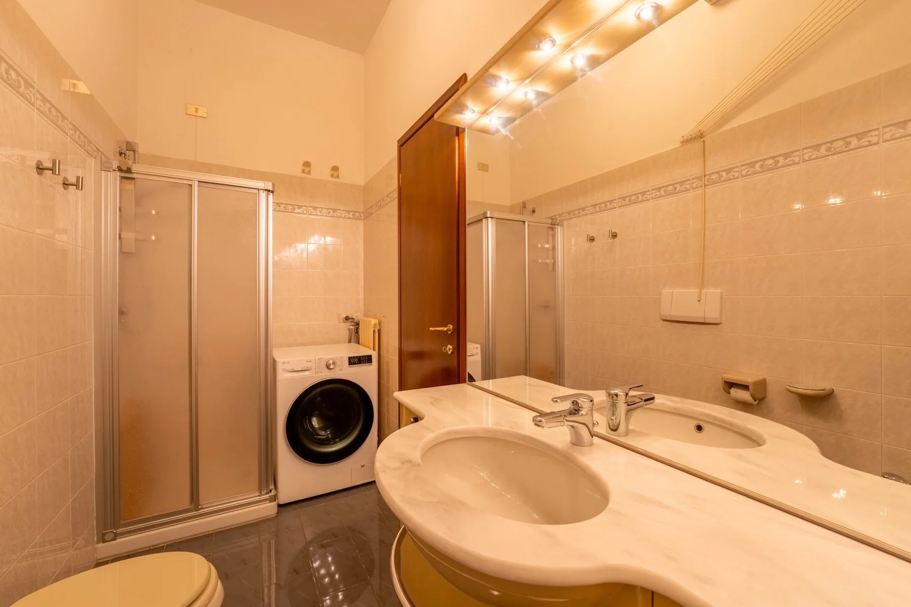 Un baño alicatado con ducha, lavadora y lavabo doble.