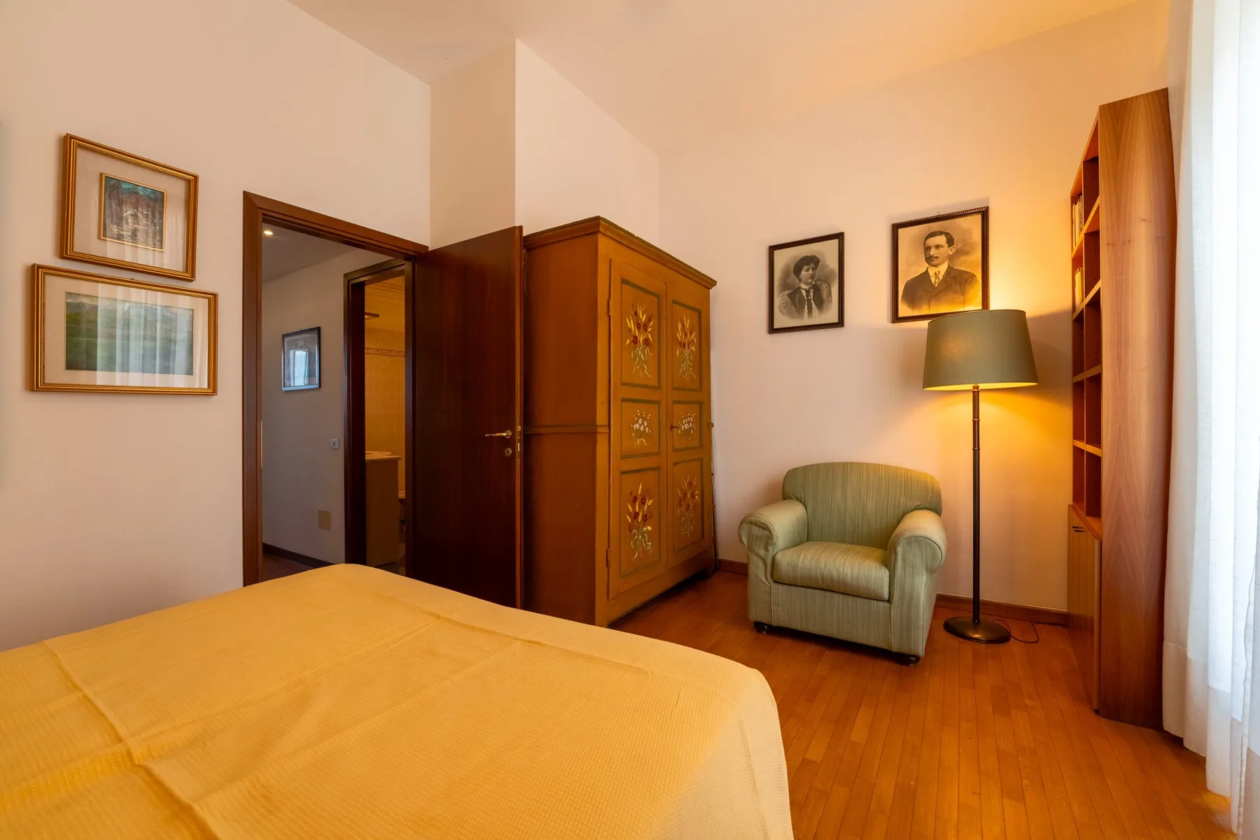 Un dormitorio con una cama, un sillón y una lámpara de pie encendida.