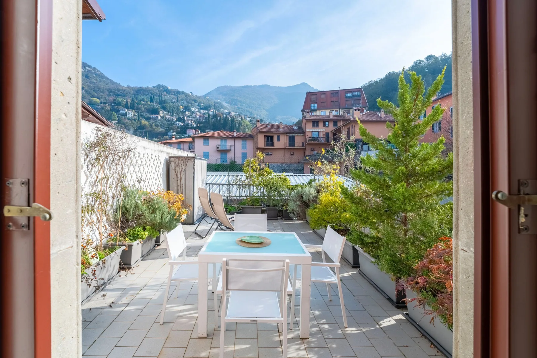 Una terraza en la azotea con mesa y asientos da a edificios en la ladera.