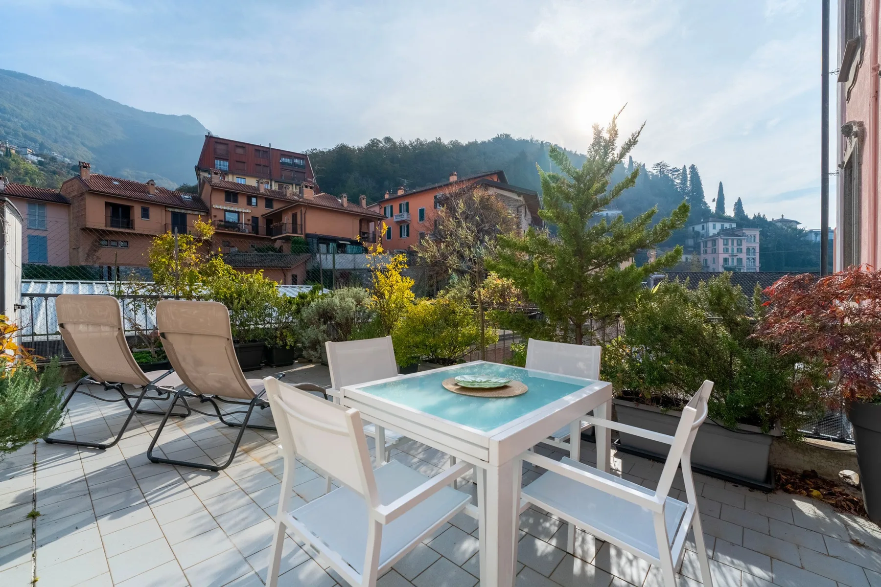 Una terraza tiene asientos al aire libre y una mesa con edificios y colinas al fondo.
