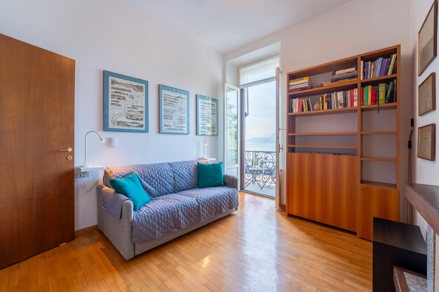 Una sala de estar con sofá, estantería y puerta acristalada que da a un balcón.