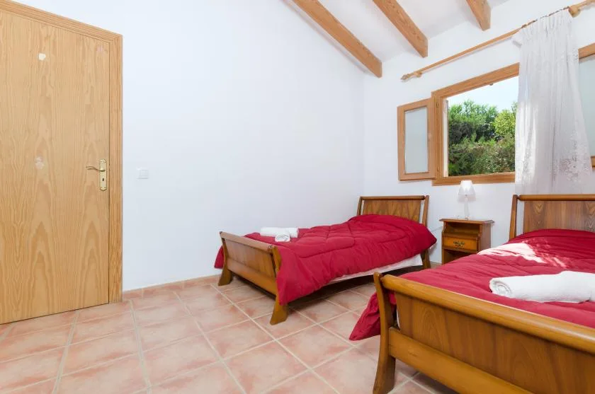 Un dormitorio con dos camas de madera vestidas con ropa de cama roja junto a una ventana abierta.