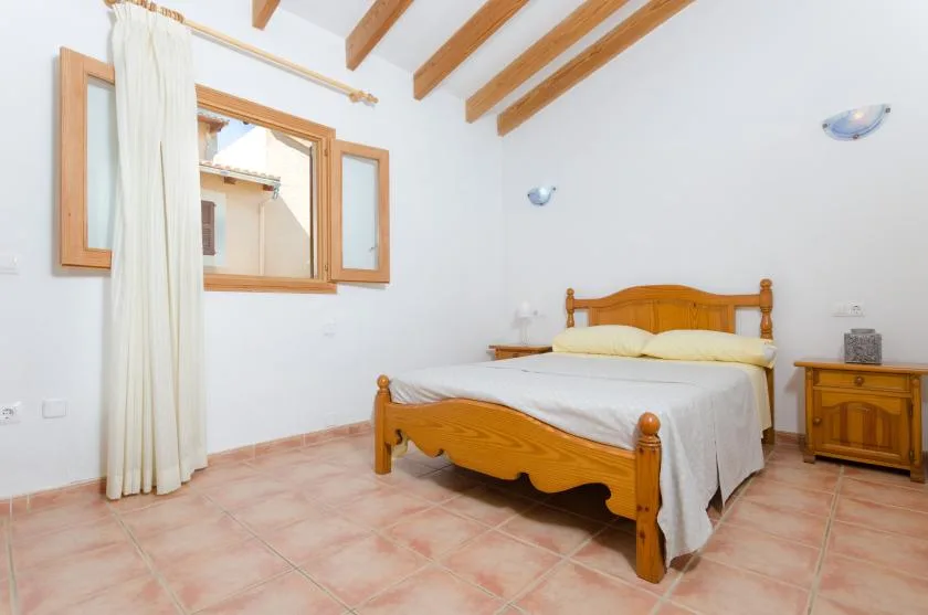 Un dormitorio con una cama de madera, suelo de baldosas y vigas vistas en el techo.