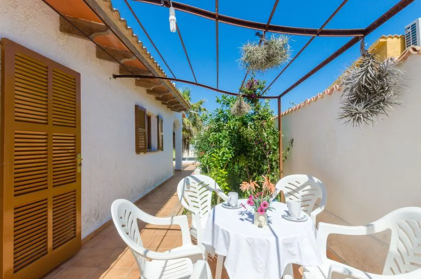 Un comedor al aire libre con una mesa redonda y asientos blancos bajo una pérgola.