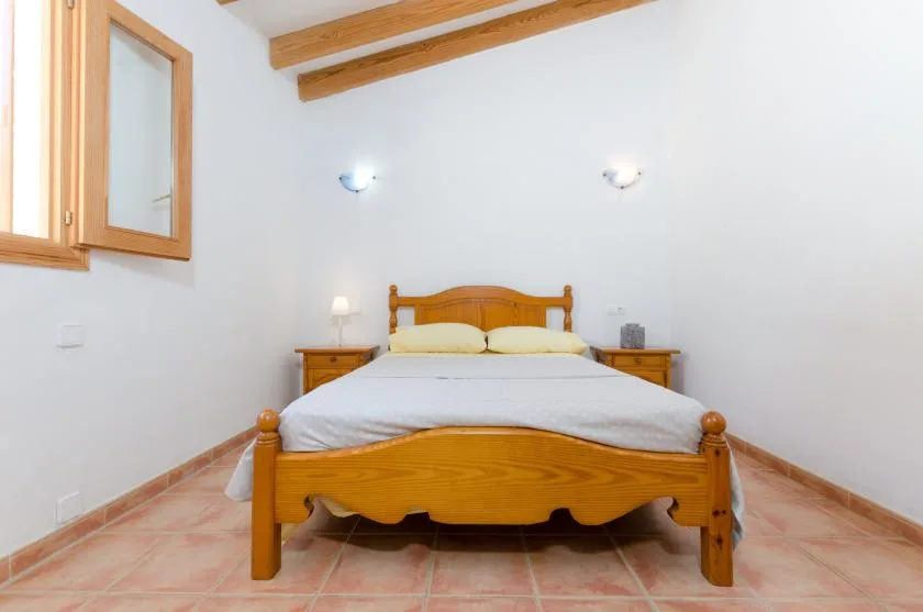 Un dormitorio con una cama de madera, mesitas de noche y vigas de techo visibles.