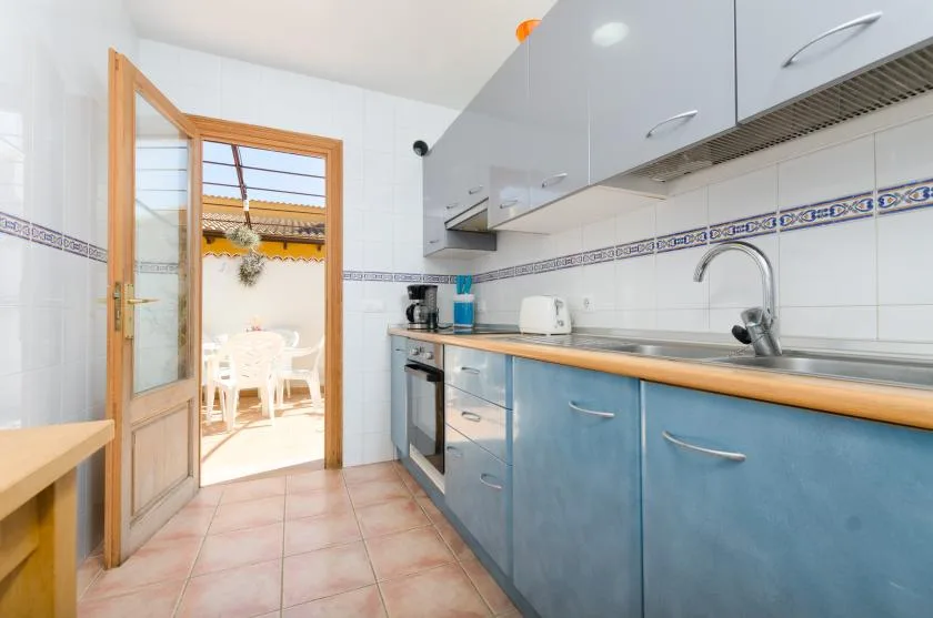 Una cocina alicatada con armarios azules, una encimera y una puerta abierta a un patio.