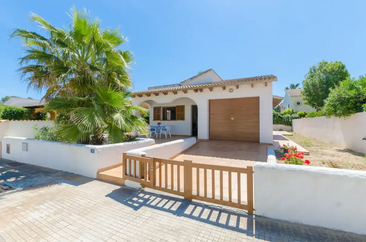 Una casa blanca de una planta con una puerta de madera y una palmera junto a la entrada.