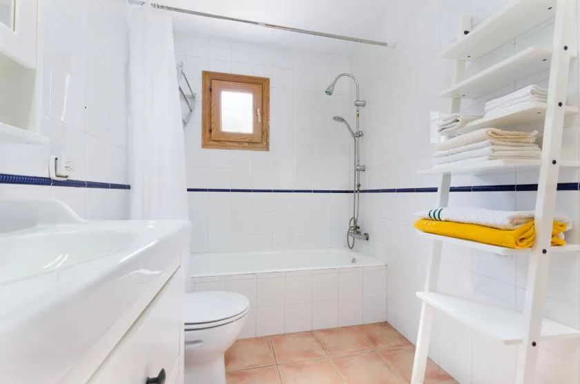 Un baño alicatado con bañera, ducha y estanterías abiertas.