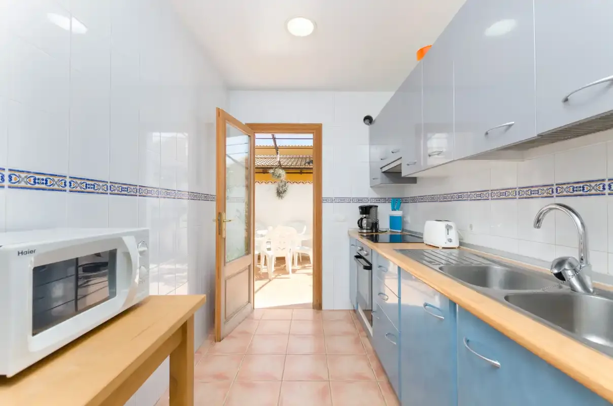 Una cocina luminosa con encimera, fregadero y una puerta abierta hacia el comedor.