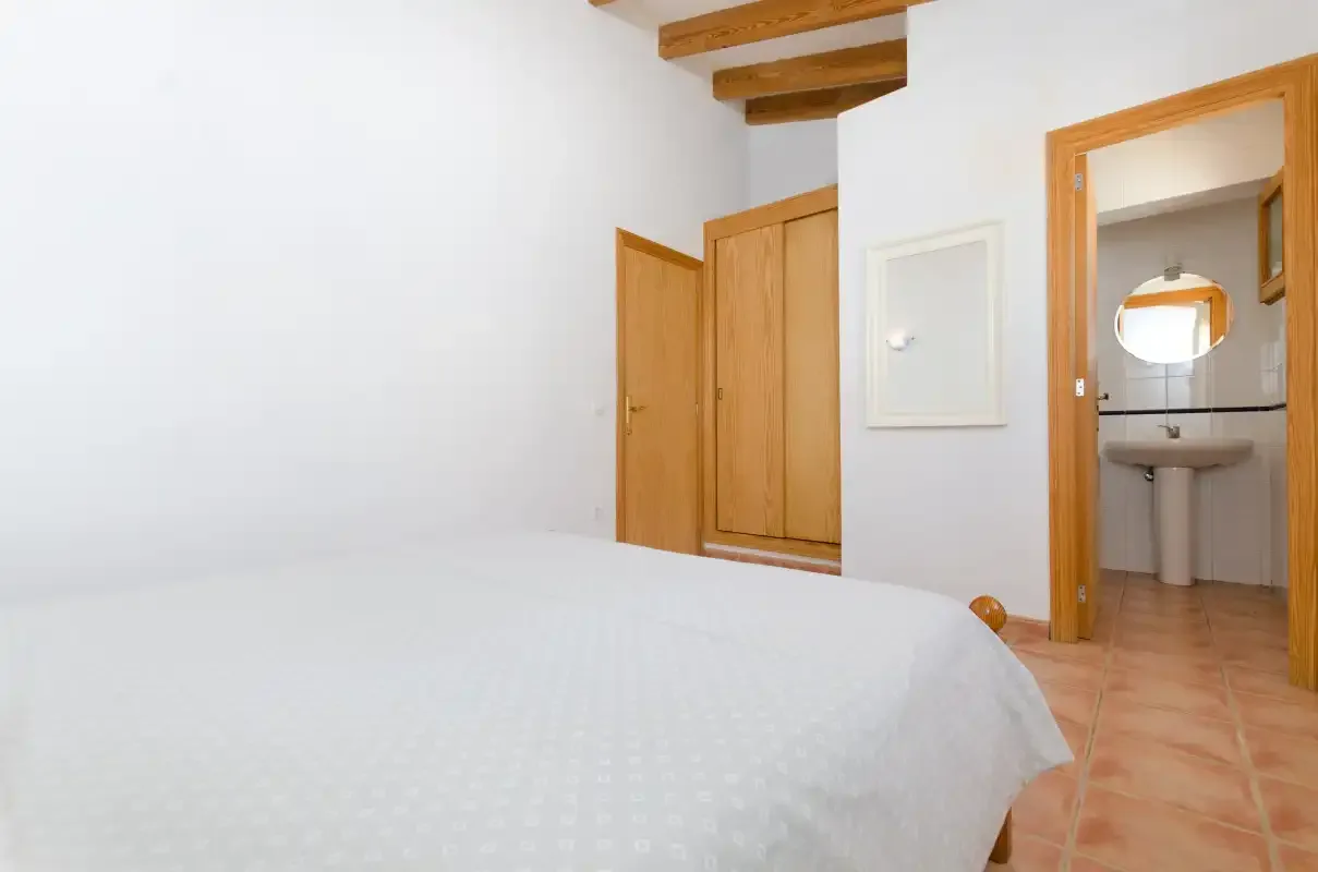 Un dormitorio con una cama en primer plano y un baño visible a través de la puerta.