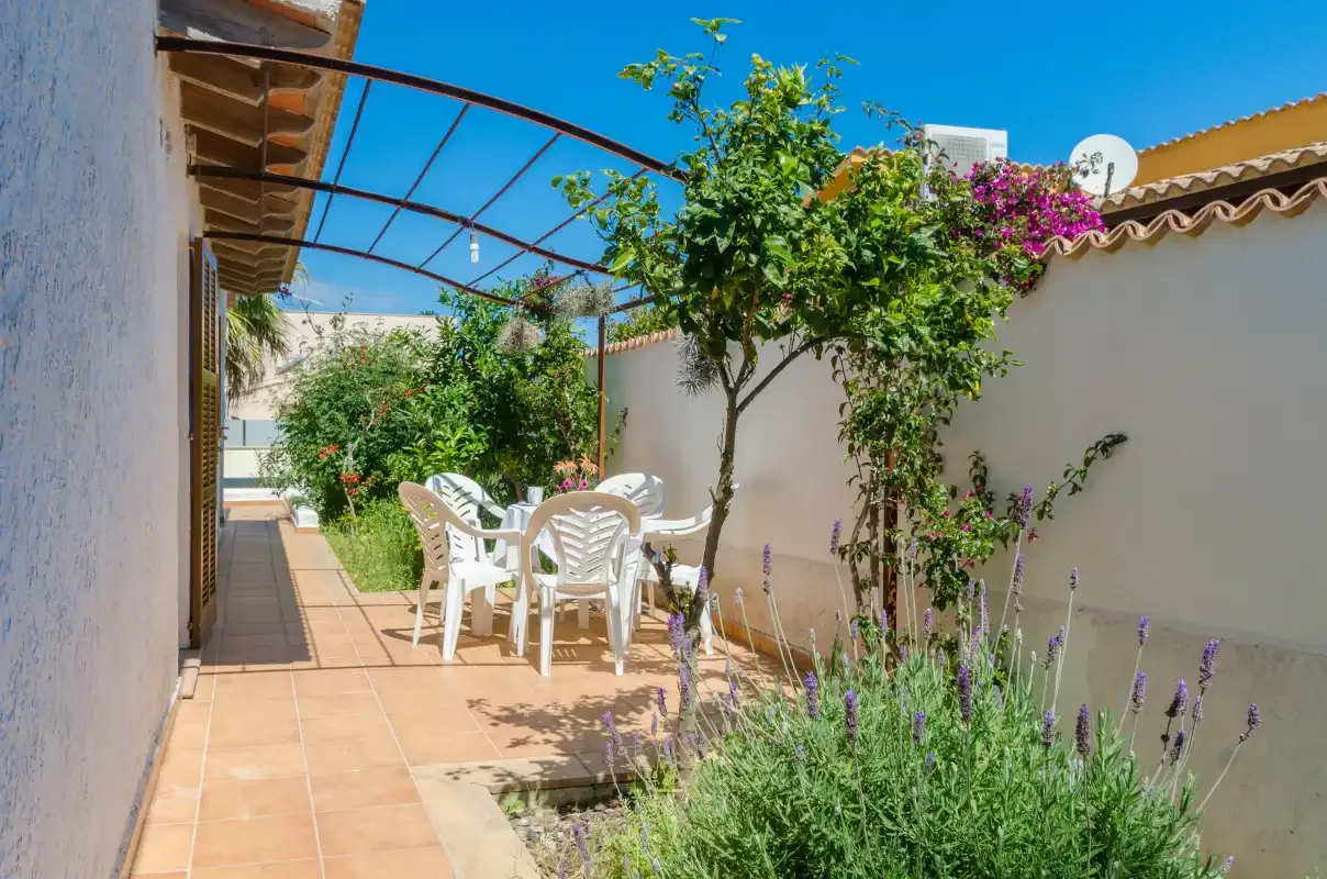 Un patio soleado con asientos al aire libre, plantas y una cubierta parcial.