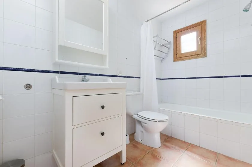 Un baño luminoso con azulejos, lavabo, inodoro y bañera.