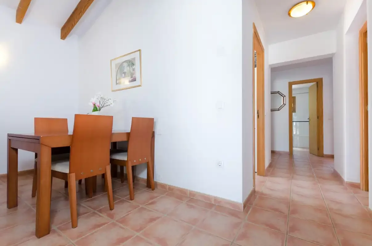 Un comedor con asientos de madera junto a un pasillo de suelo embaldosado.
