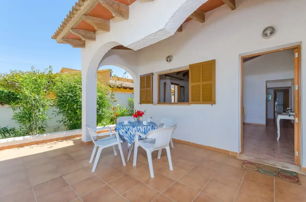 Un patio cubierto con una mesa y sillas junto a una puerta abierta.