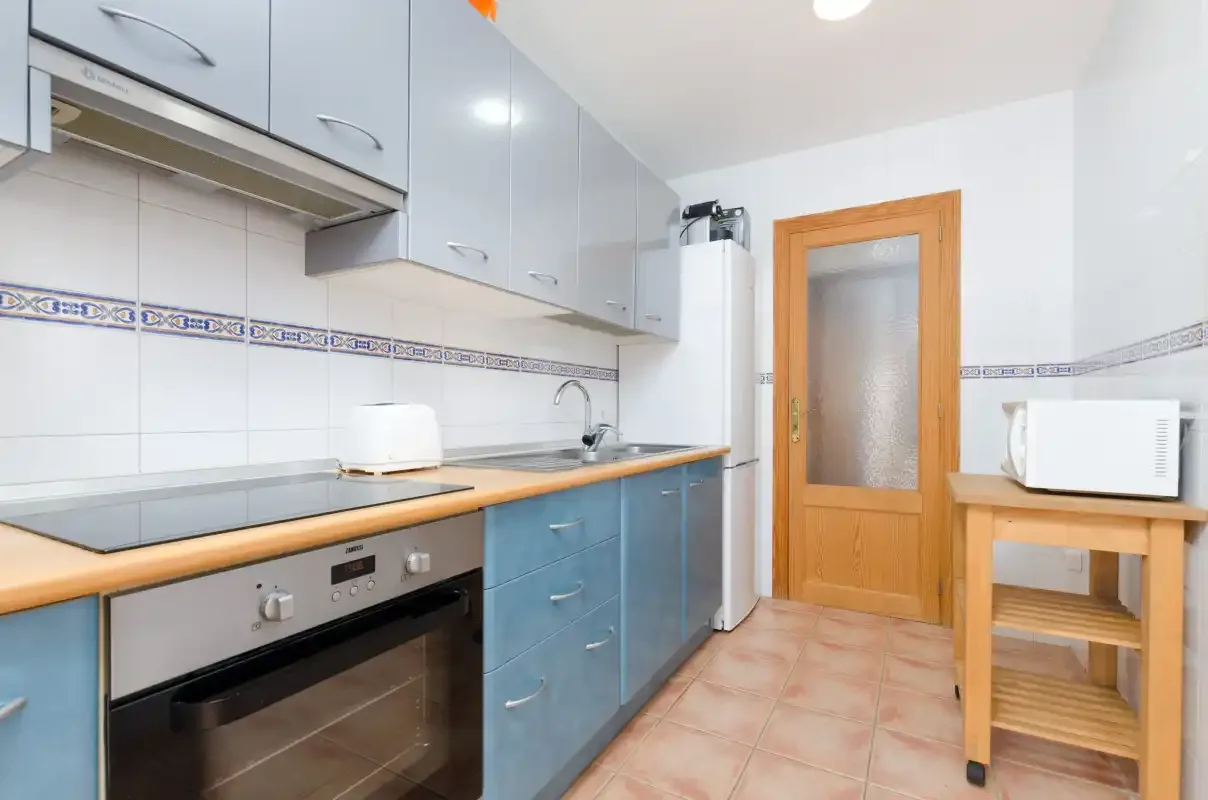 Una cocina compacta con armarios azules, horno de encimera y una puerta de madera.